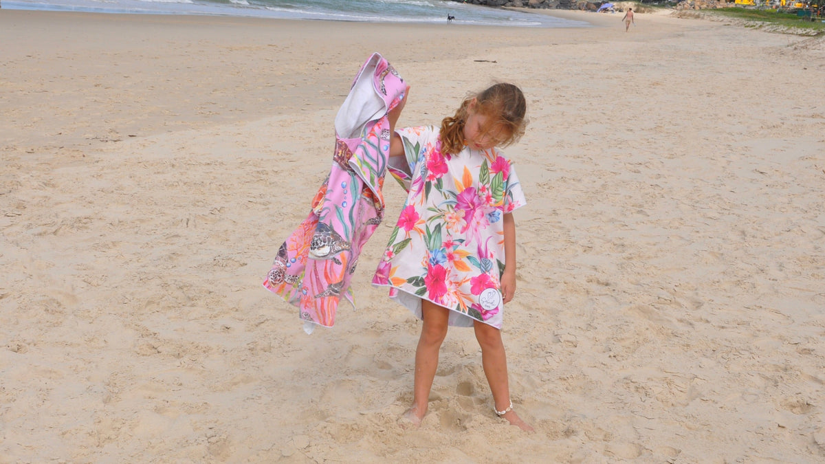 Girl wearing Turtle Cove sand free hoodie shaking out the sand from a Island Princess medium