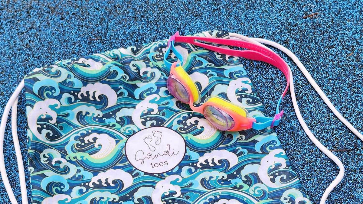 Sandi Toes Wipeout Sand Free Hoodies are synonymous with swimming and surf showing in this picture a set of goggles and a Sandi Toes kids back pack .jpg